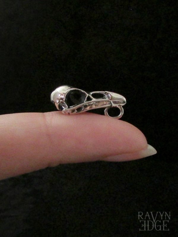Tiny sculpted raven skull charm on a finger to show size
