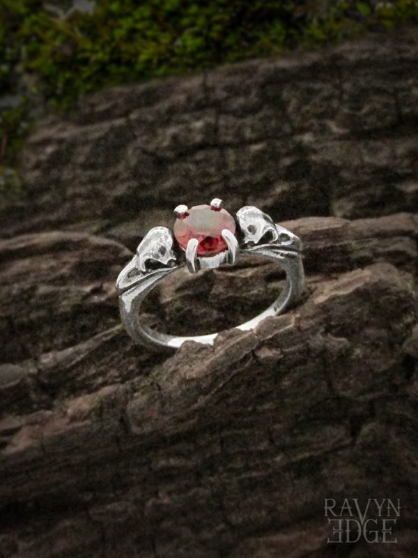 Two raven skulls on a dainty garnet wedding ring